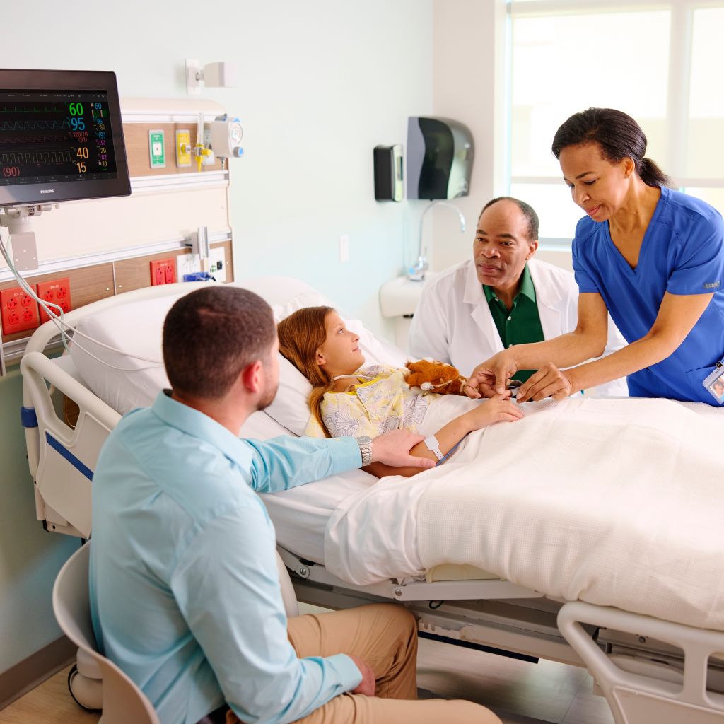 A young patient with a glove finger SpO2 sensor is surrounded by nurse, doctor and family member.  