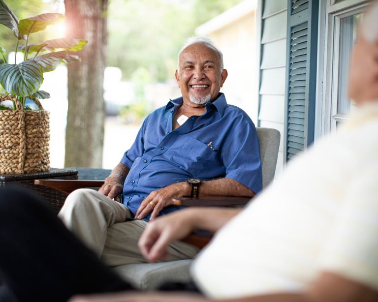 A man sits on his front porch at home while being monitored with a Philips Cardiac Ambulatory Monitoring device.