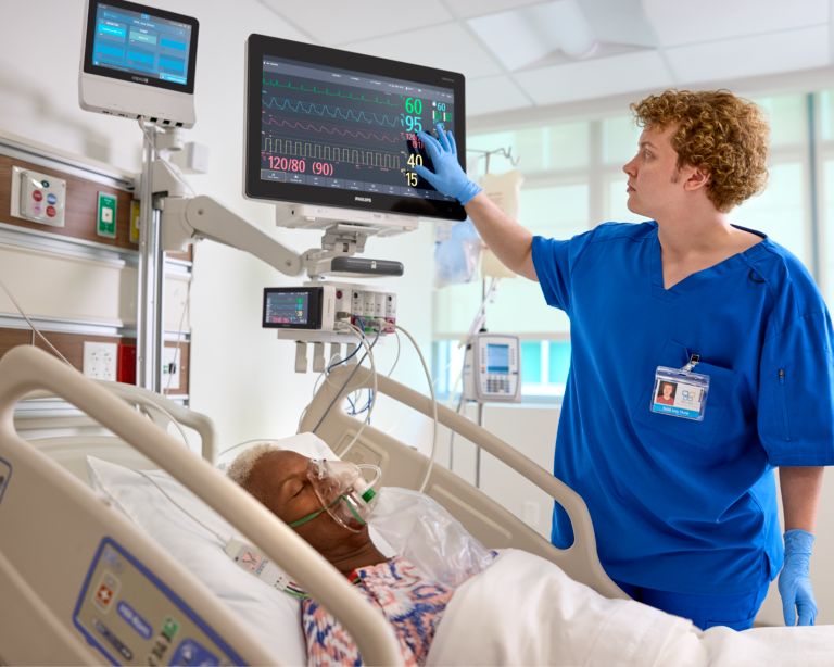 A nurse uses a patient monitor on a patient in bed 
