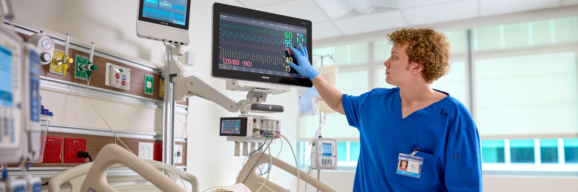 A nurse uses a patient monitor on a patient in bed