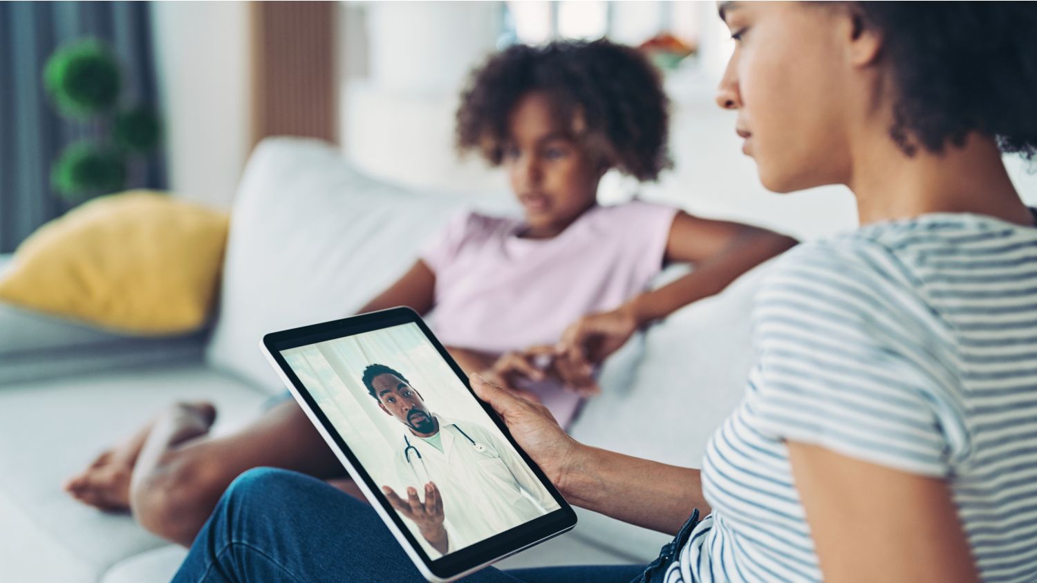 An image of a woman on couch having a telehealth visit with doctor on a tablet