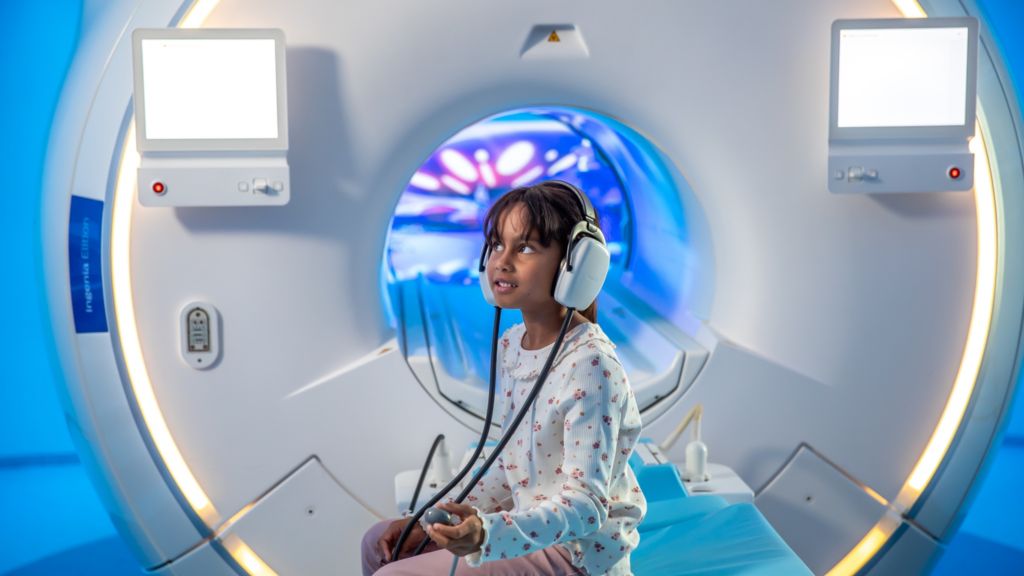 A pediatric patient sits on a scanning bed
