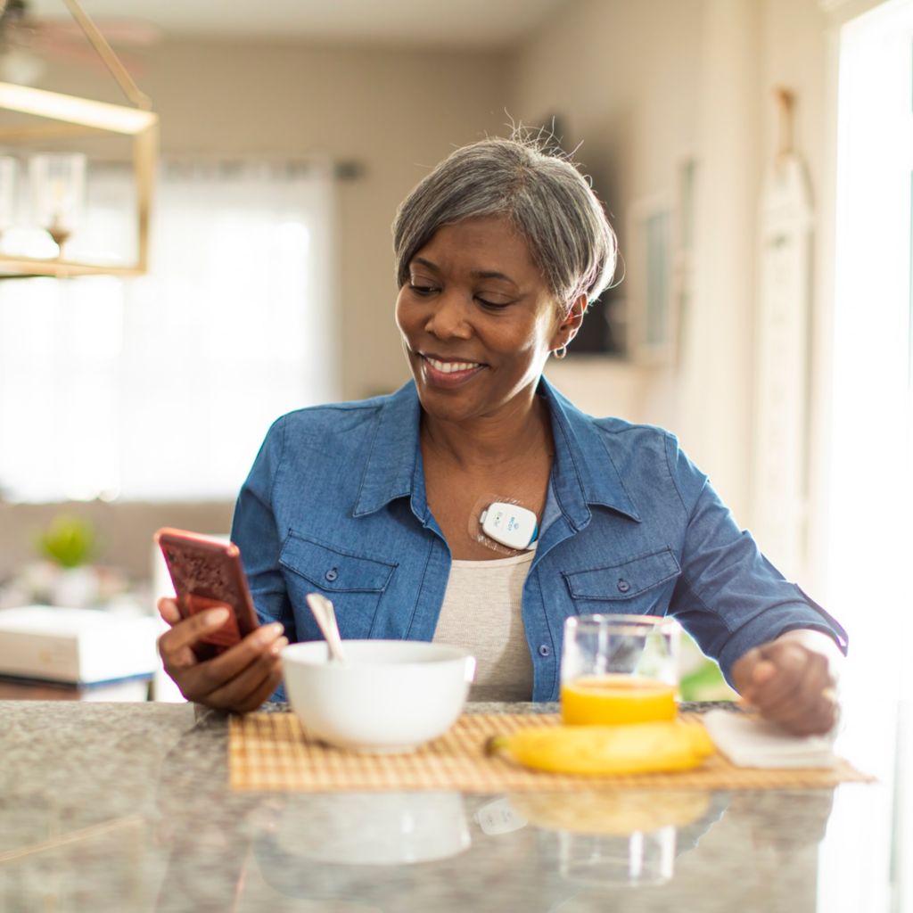 A woman looks at her phone at home while wearing Philips Mobile Cardiac Telemetry – MCOT.