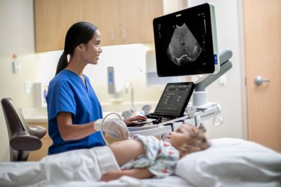 Clinician performing abdominal ultrasound scan on child using ultrasound system
