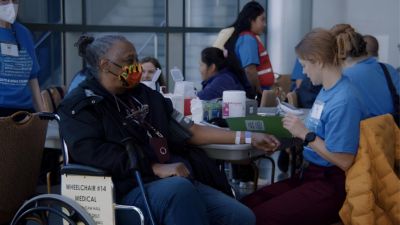 Patient in wheelchair receiving blood pressure check from volunteer clinician