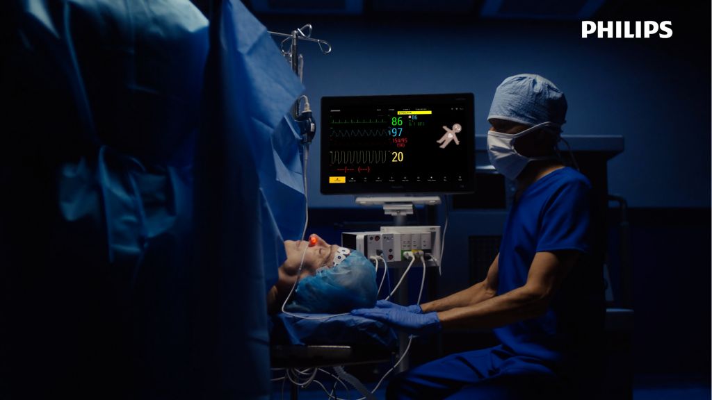 The patient lies on the operating room table for her procedure as Philips Visual Patient Avatar is shown on a monitor.