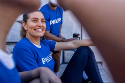 A small group of adults wearing blue Philips branded athletic shirts relax on outdoor steps