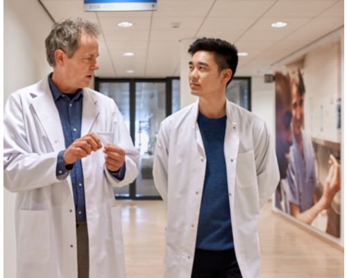 a man in white lab coats talking to another man in a hallway