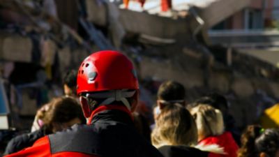 Rescue workers in red helmets assisting people near collapsed buildings after earthquake