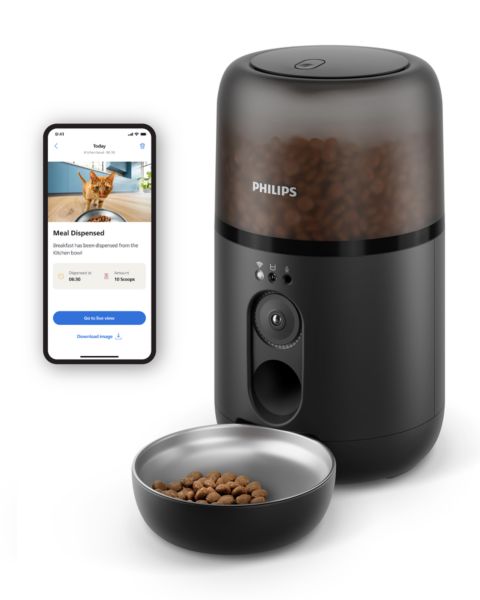 Comedero inteligente de Philips en negro mate con cámara tras dispensar comida seca junto a una demostración en la pantalla del teléfono de la aplicación Pet Series