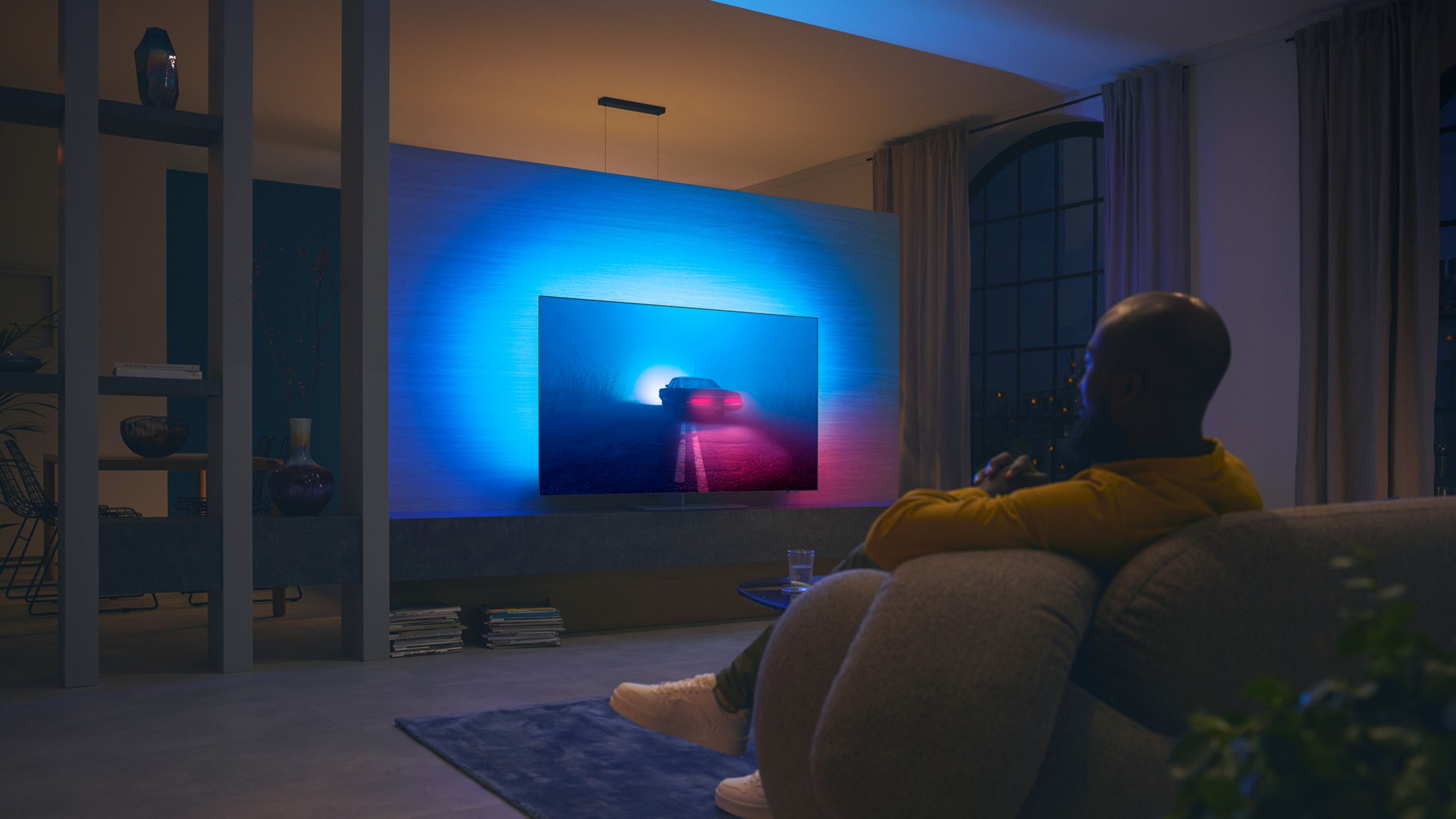 Person watching a Philips Ambilight TV, with blue and red ambient light on the wall.