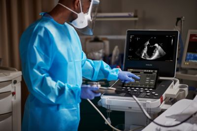 Clinician in protective gown operates Philips ultrasound system displaying cardiac image in hospital