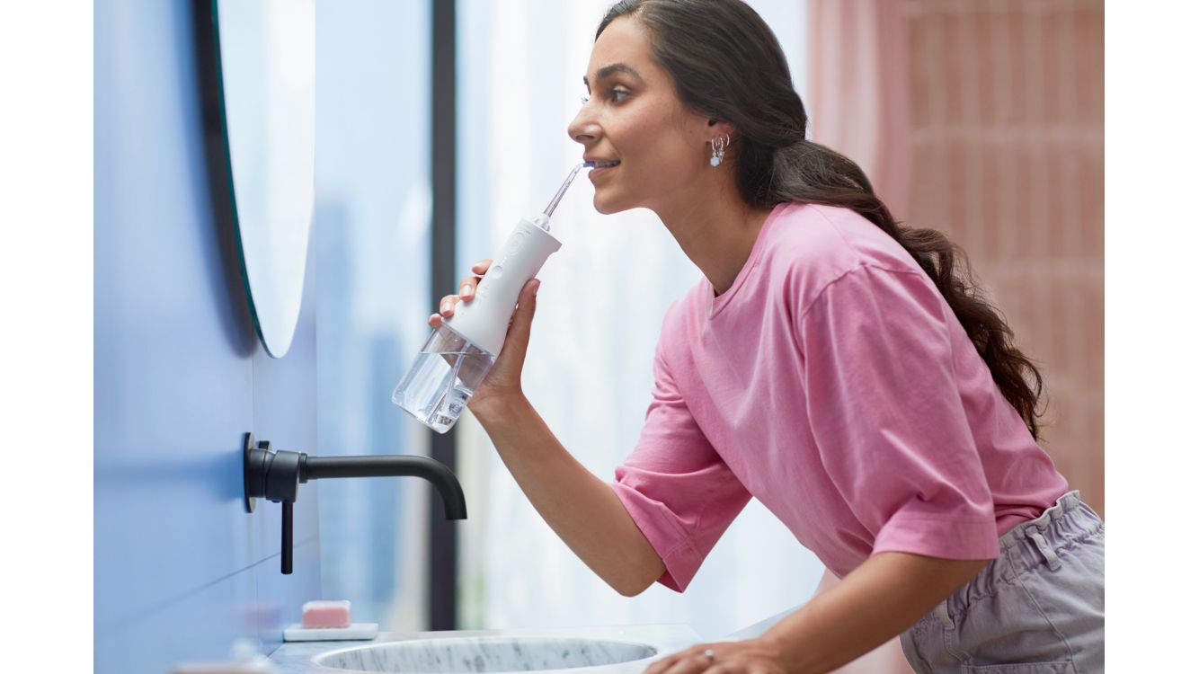 En kvinde kigger væk fra kameraet, mens hun børster sine hvide tænder med en elektrisk Sonicare Airfloss-tandbørste fra Philips.