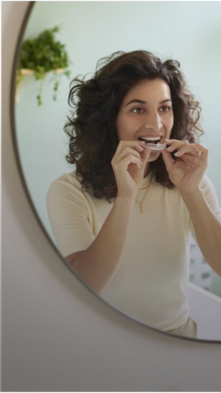 A woman looking in a mirror while placing a Sonicare whitening kit tray in her mouth