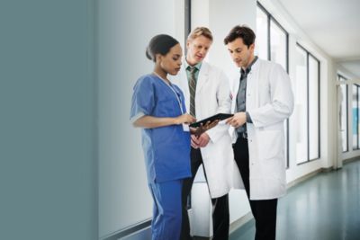 A nurse and two doctors reviewing information on a tablet in a hospital corridor