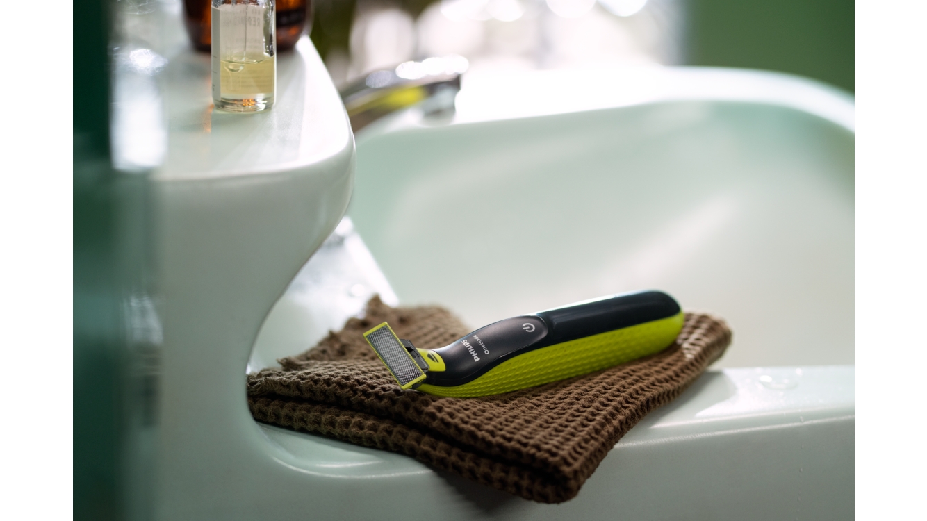 Philips OneBlade laying on top of a  brown hand towel placed on the side of a bathroom sink.