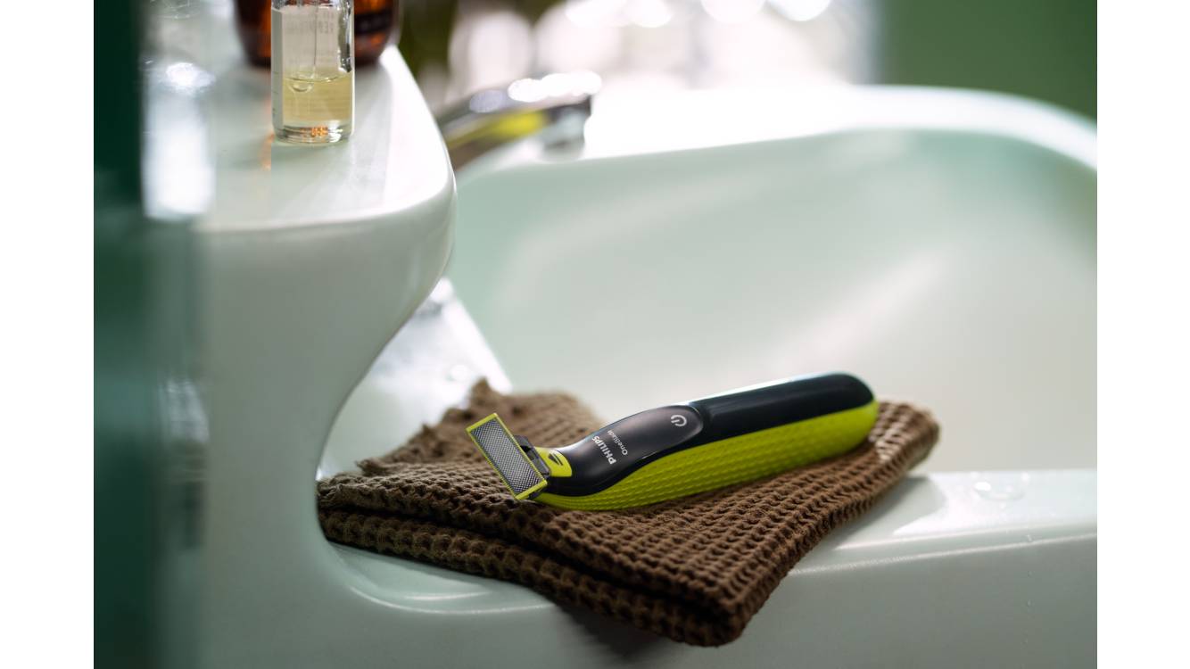 Un Philips OneBlade è appoggiato su un asciugamano marrone sul bordo del lavandino del bagno.