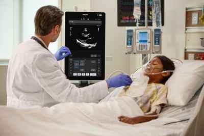 Clinician using Philips ultrasound system to examine a pediatric patient in a hospital bed
