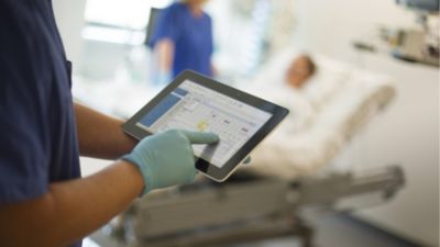 Nurse reviewing patient data on tablet in hospital room
