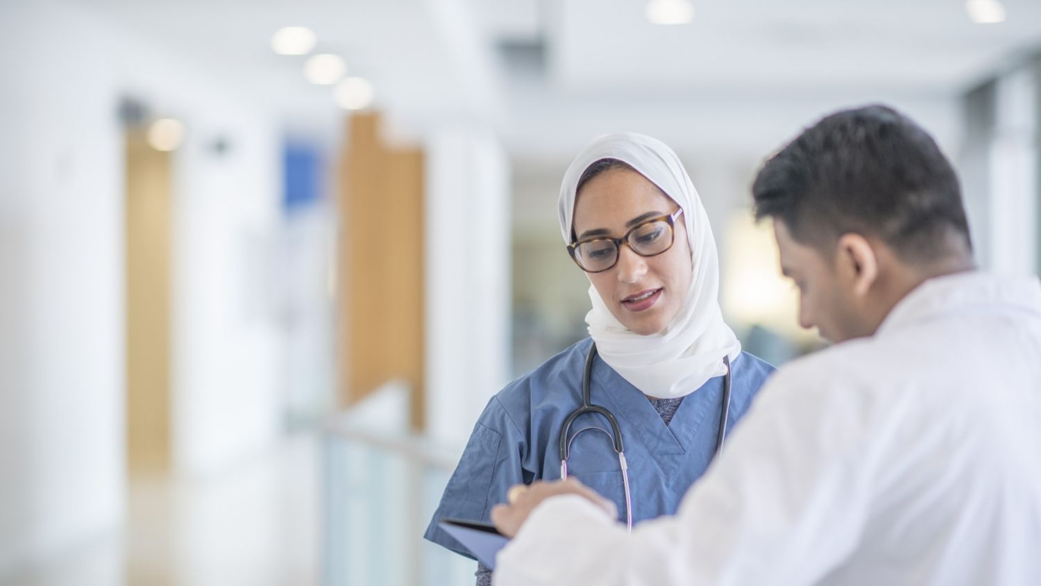 Female healthcare professional in a hijab consulting with a patient in a hospital corridor