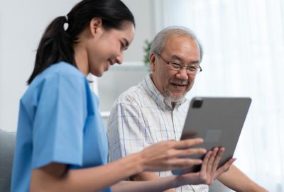 Pengasuh menunjukkan sebuah tablet kepada seorang pria lanjut usia selama kunjungan ke rumah