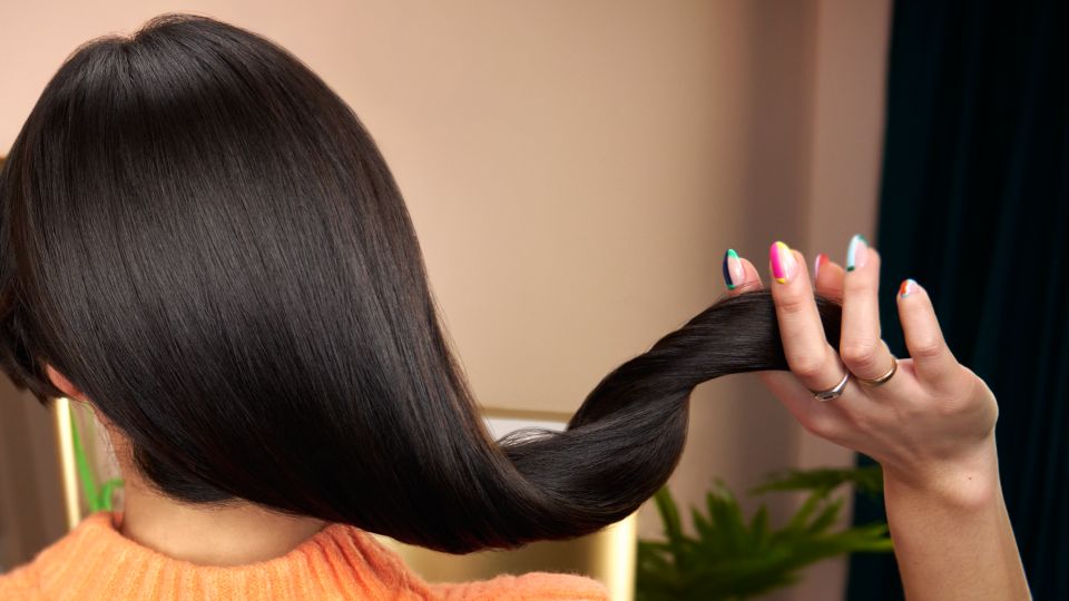 Eine Frau fährt sich mit den Fingern durchs Haar, nachdem sie sich zu Hause professionell die Haare geföhnt hat.