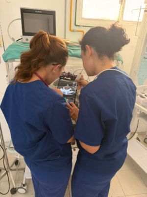 Two healthcare professionals review ultrasound images on a tablet beside an infant incubator.