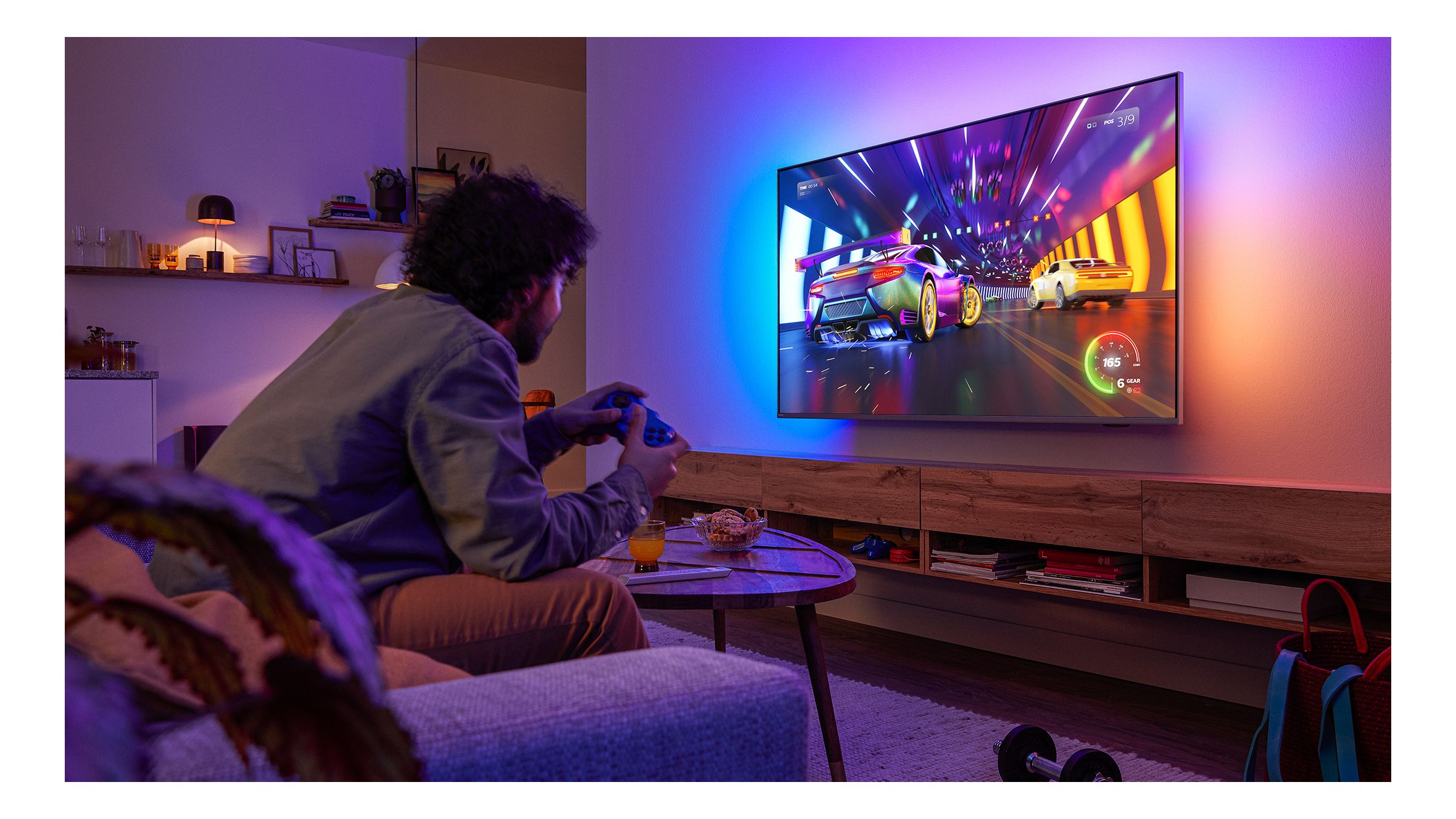 A racing video game is displayed on a Philips Ambilight TV in a dimly lit room