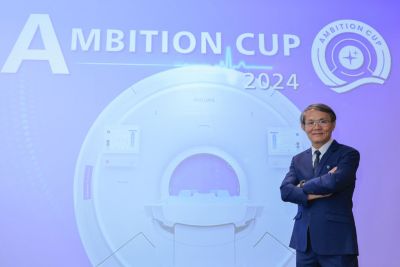 วิโรจน์ วิทยะเวโรจน์ ยืนอยู่ด้านหน้าป้ายจัดแสดงเครื่อง MRI ในงาน Ambition Cup 2024 ณ งานนวัตกรรมด้านการดูแลสุขภาพ