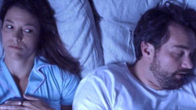 Couple lying in bed with one partner awake while the other sleeps