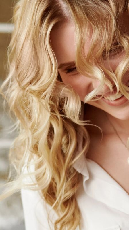 Junge Frau mit blonden Locken blickt lachend nach unten.