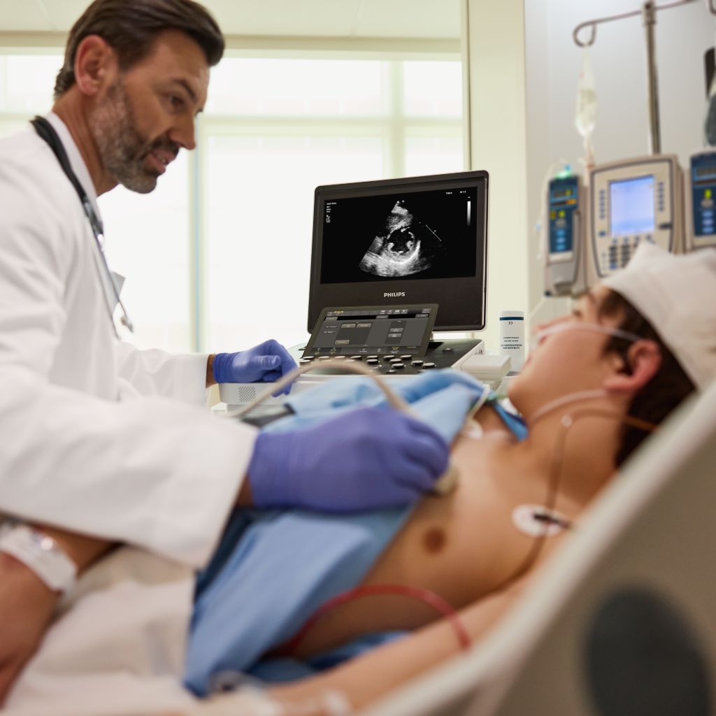 Clinician performing cardiac ultrasound imaging on pediatric patient in critical care setting.