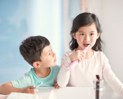 A boy watching a girl use her Sonicare For Kids power toothbrush