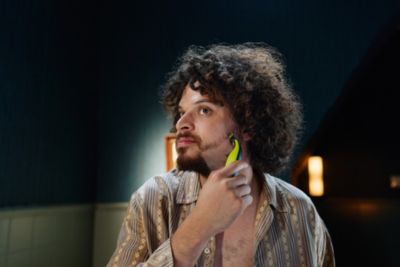 Un homme avec des cheveux boucl&eacute;s bruns utilise le Philips OneBlade pour se raser la barbe.