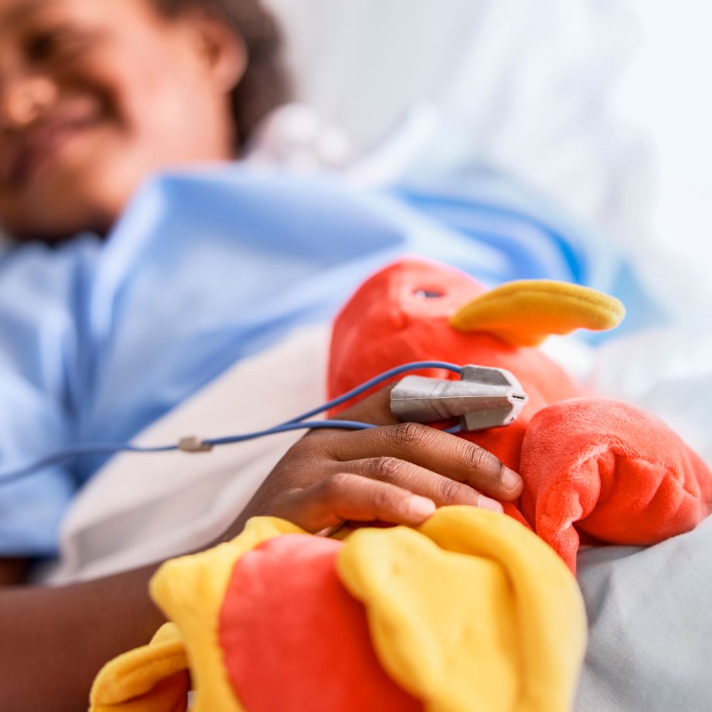 patient smiles in bed with SpO2 sensor and stuffed dragon toy