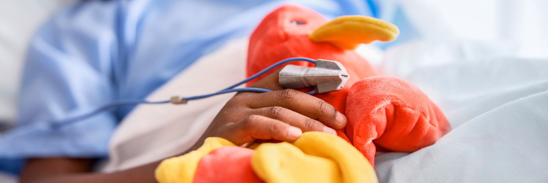 patient with spO2 sensor in bed holding a stuffed animal