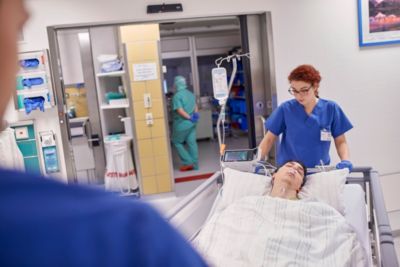 Nurse transporting patient on hospital bed with vital signs monitor