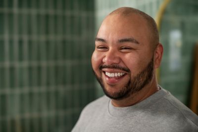A bald man in a grey shirt smiling at the camera.