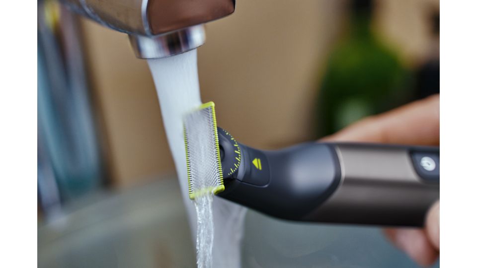 A Philips OneBlade Pro is rinsed under a running tap.