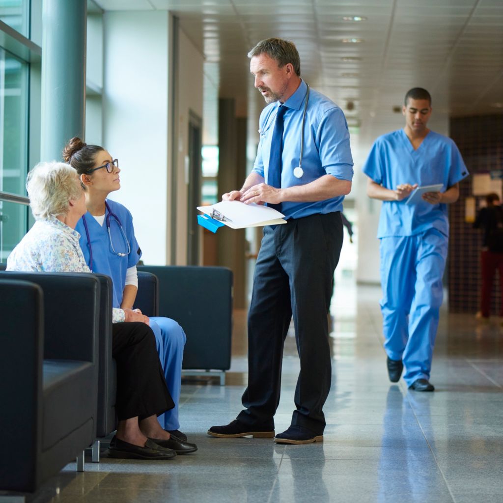Doctor and consultant talking to patient in hospital corridor 