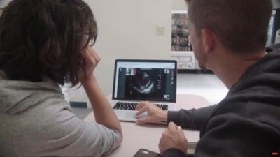 Two people reviewing ultrasound exam remotely on laptop for telehealth training