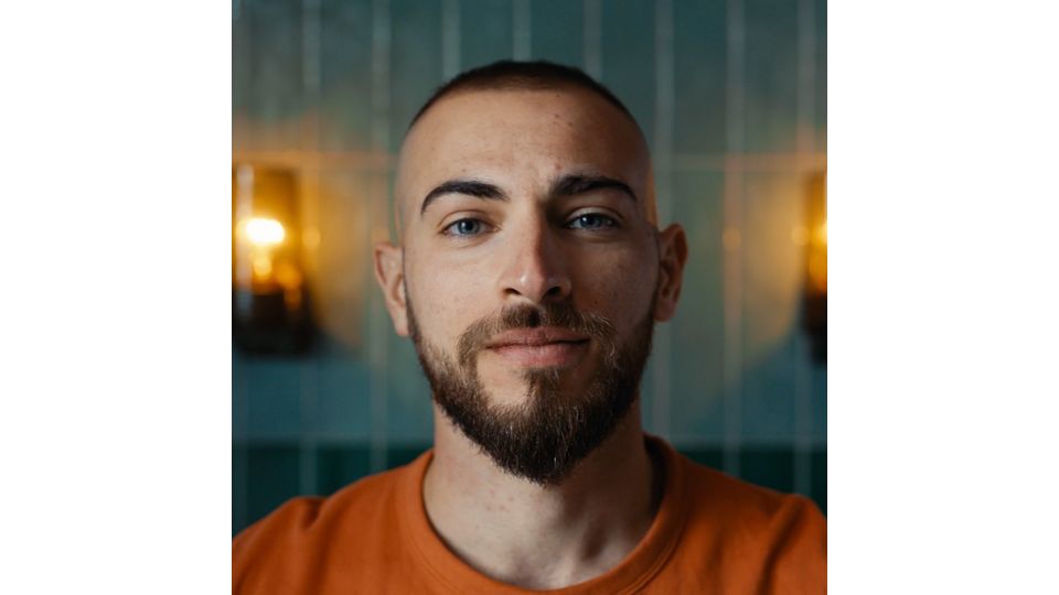 Close up of a black man in a white shirt and grey cardigan and his chin puff beard.