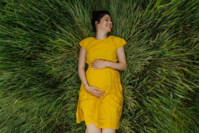 Mulher grávida deitada na grama com um vestido amarelo, segurando a barriga ao ar livre
