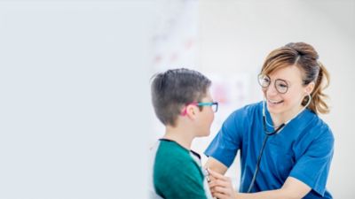 A smiling healthcare professional using a stethoscope while speaking with a young boy wearing glasses.