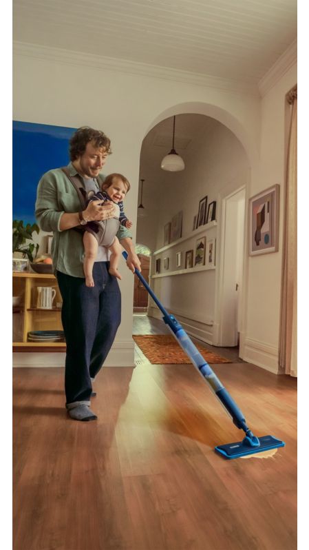 Muškarac koji drži bebu briše drveni pod u svijetloj