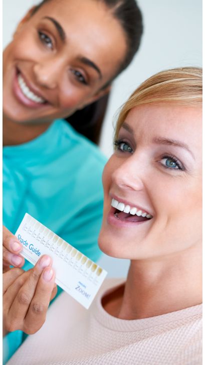 Smiling patient holding a shade guide close to her smile