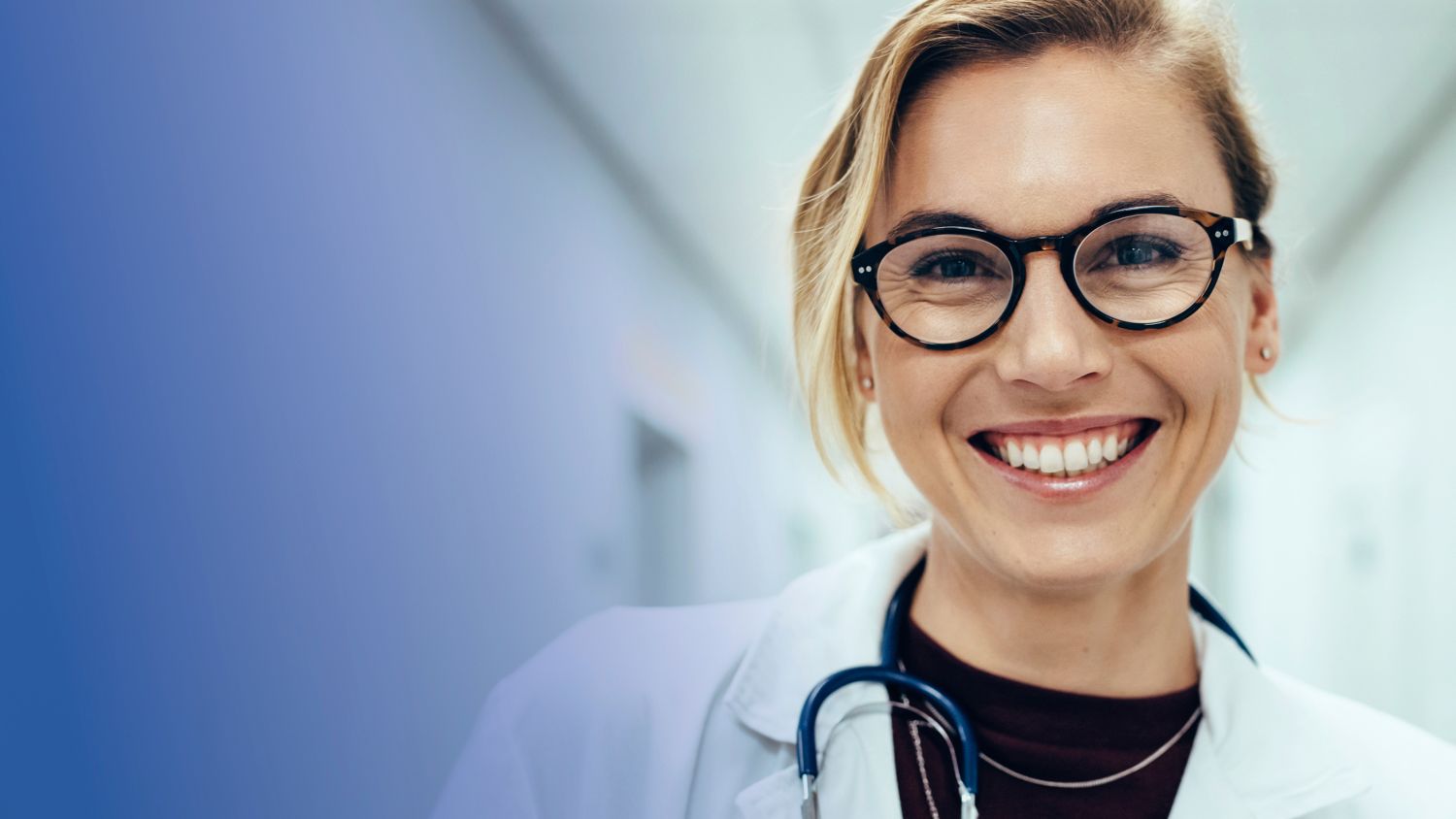 Lächelnde Ärztin mit Brille und Stethoskop in einem Krankenhausflur