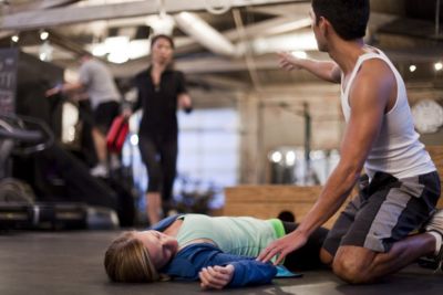 Person assisting woman during cardiac emergency in gym while calling for help