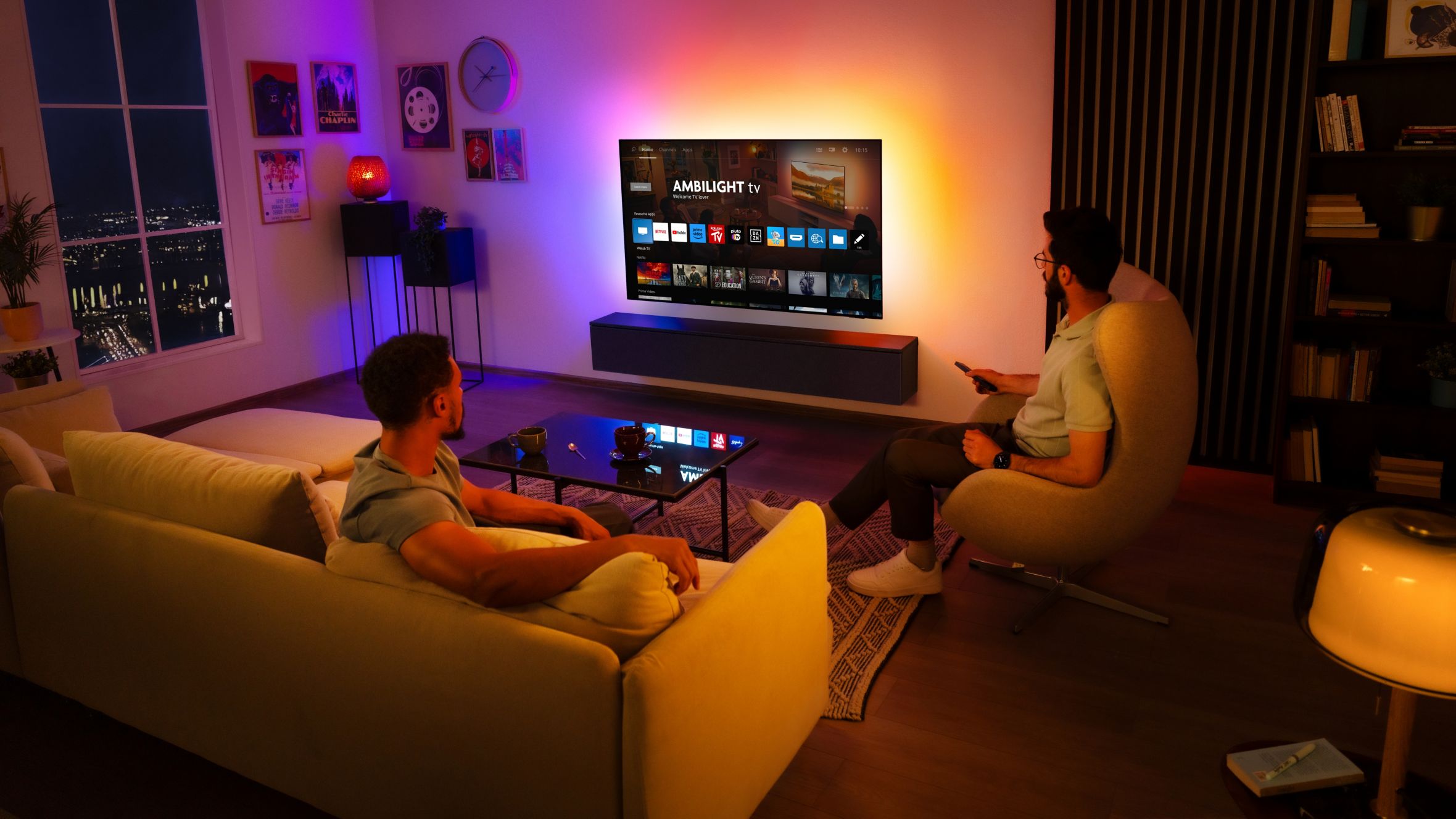 Two men watch a wall-mounted Ambilight TV in a living room