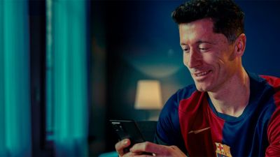 Person nutzt Smartphone mit eingeschaltetem Ambilight-TV im Hintergrund